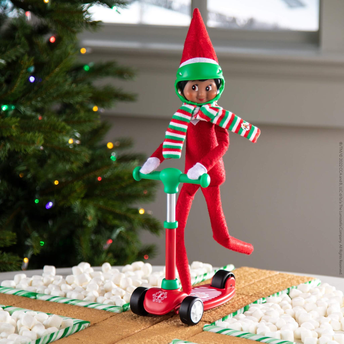 elf on the shelf op een scooter step met helm en gestreepte sjaal