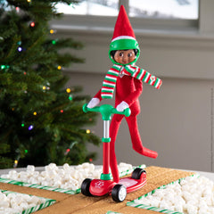 elf on the shelf op een scooter step met helm en gestreepte sjaal